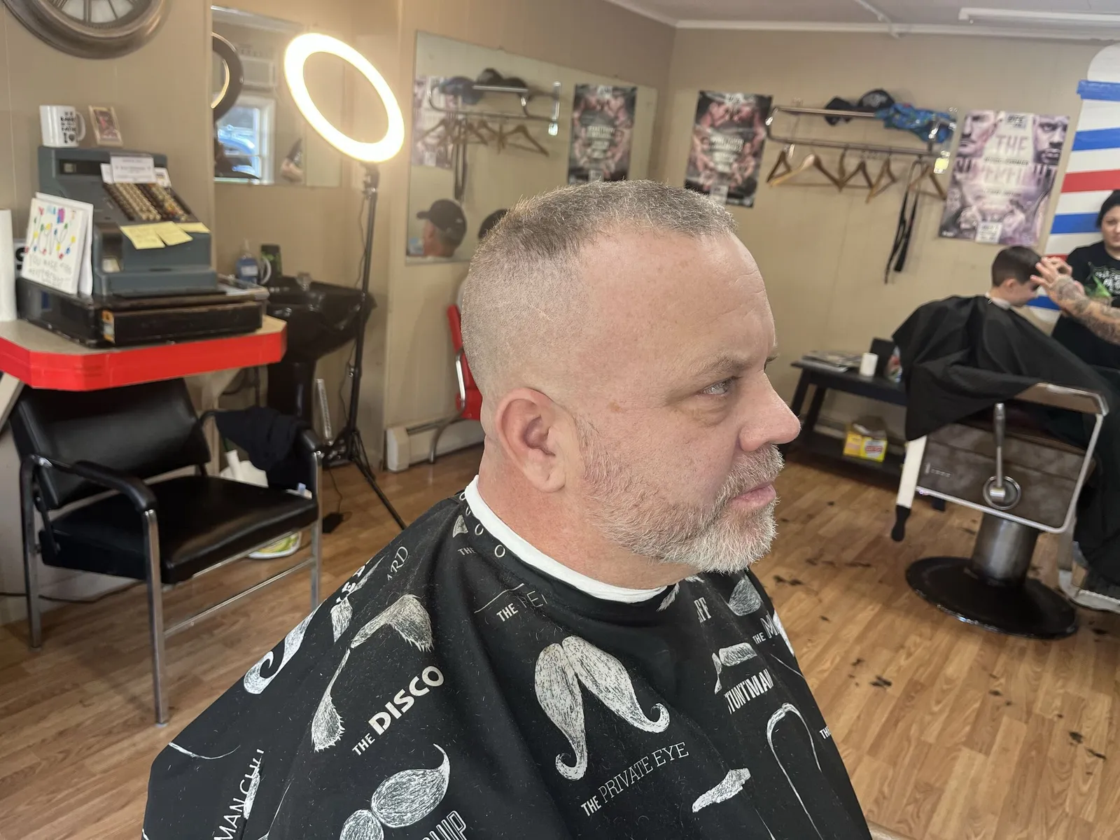 A man with a short crop, faded sides and a trimmed grey beard, inside the shop