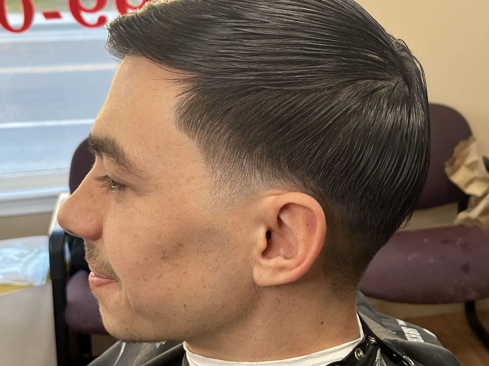 A smiling man with a slicked side part and a low fade at the temple