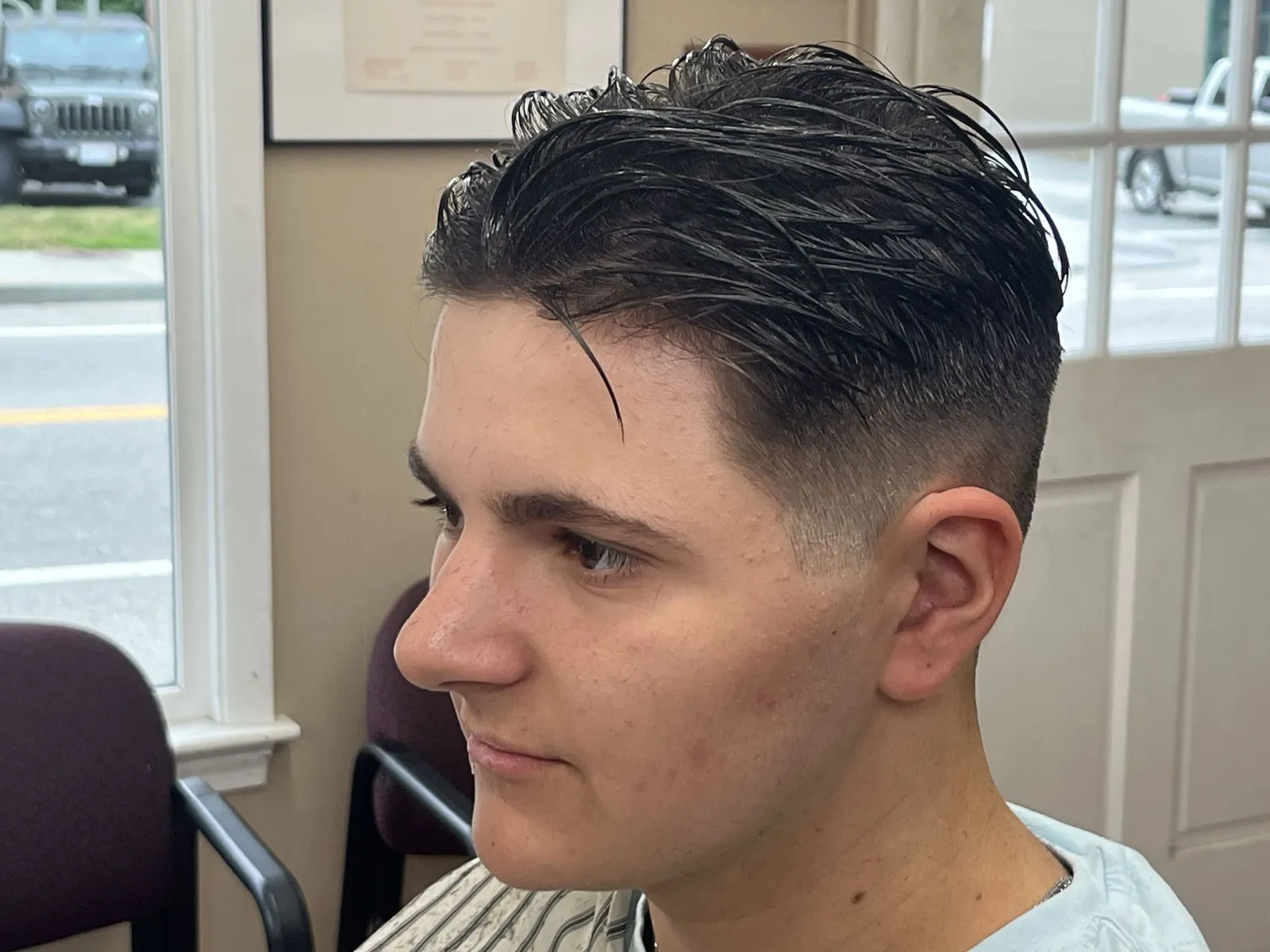 A young man with a long textured top swept to one side and a low fade