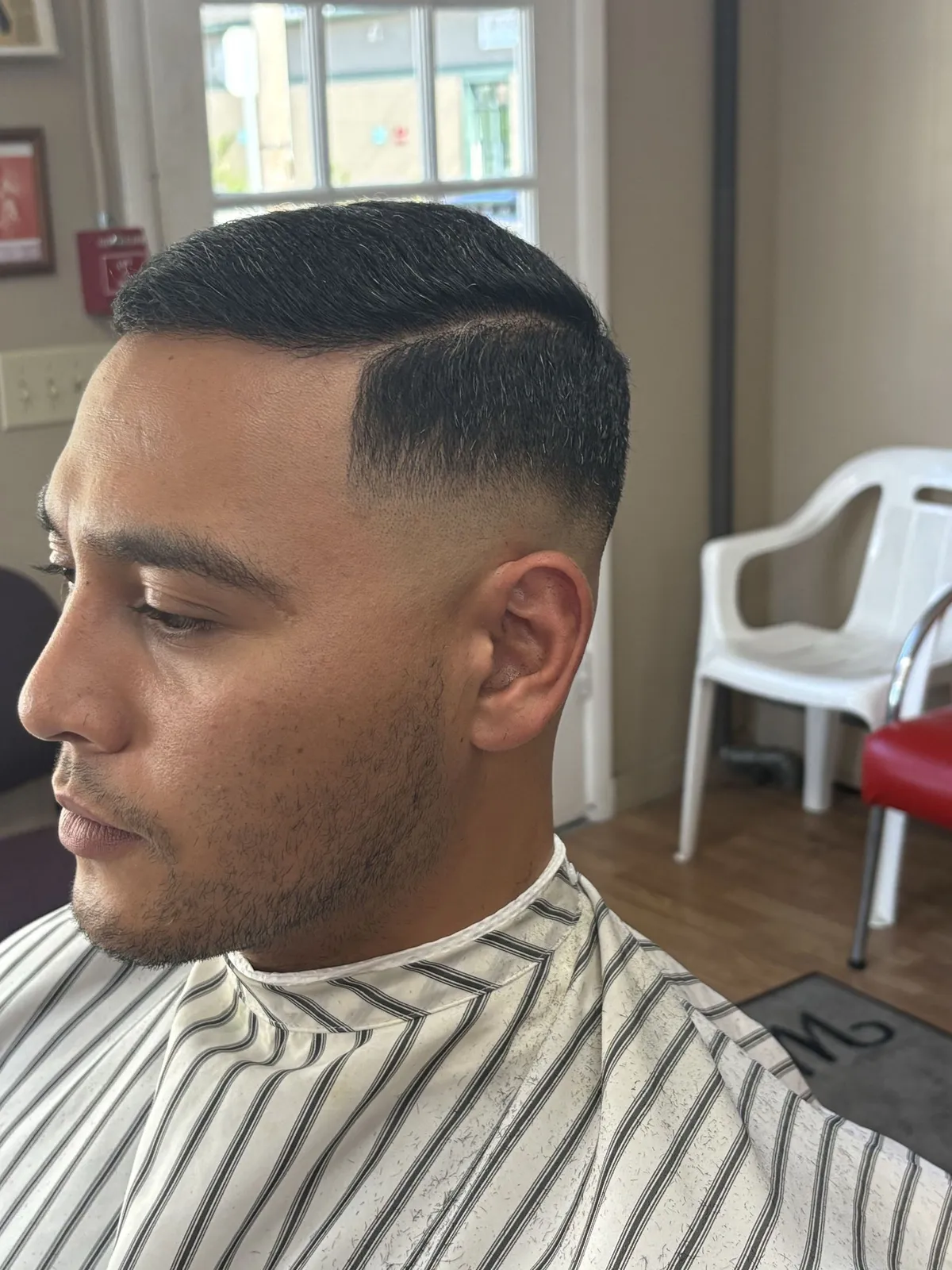 Side profile of a man with a short crop, a hard part and a mid fade