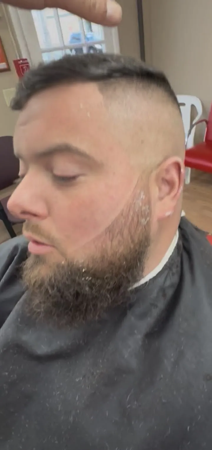 A man with a high fade on the sides and a full beard lined up with a razor
