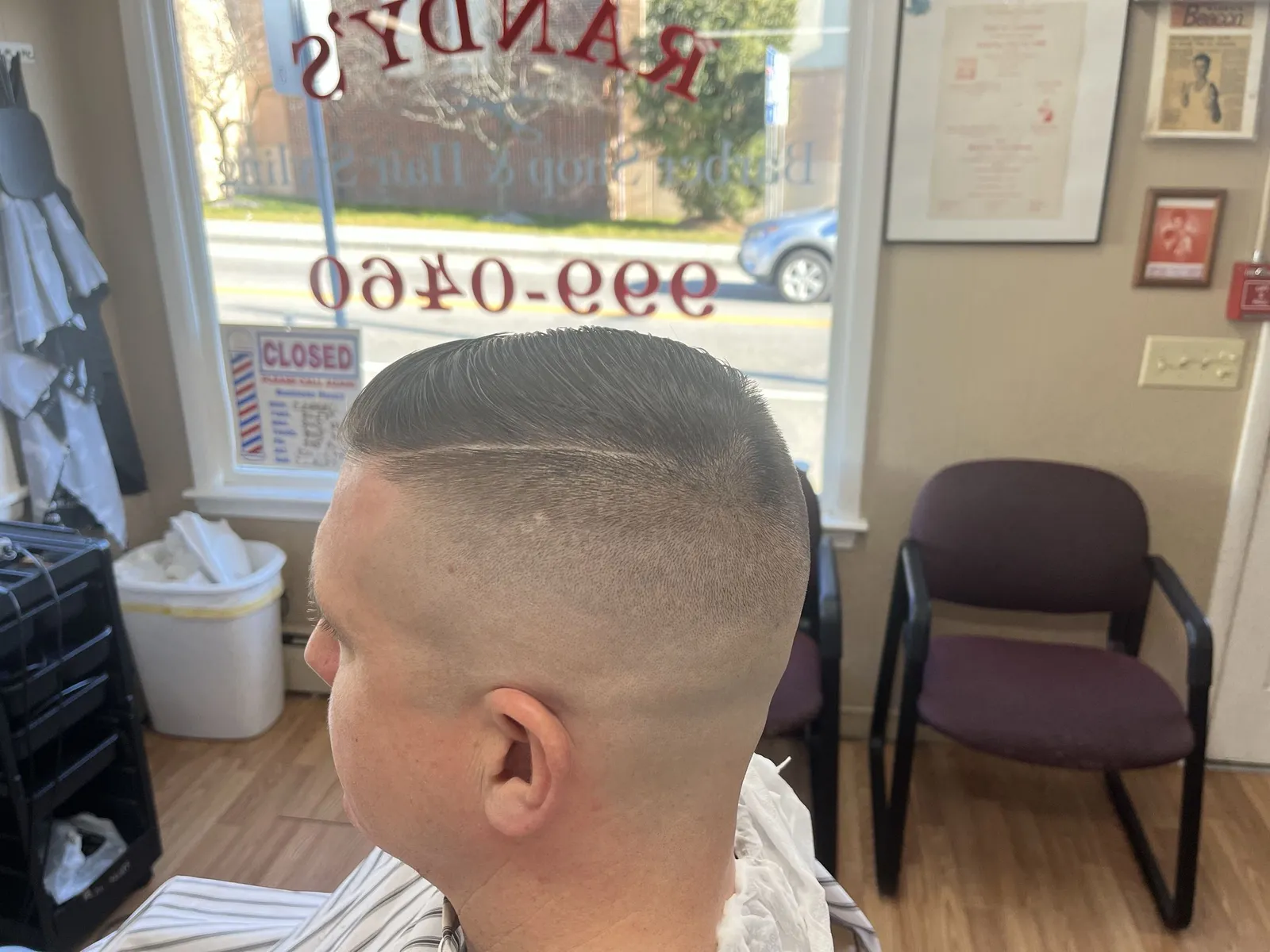 A fresh cut at Randy’s, with the shop’s window lettering and phone number behind